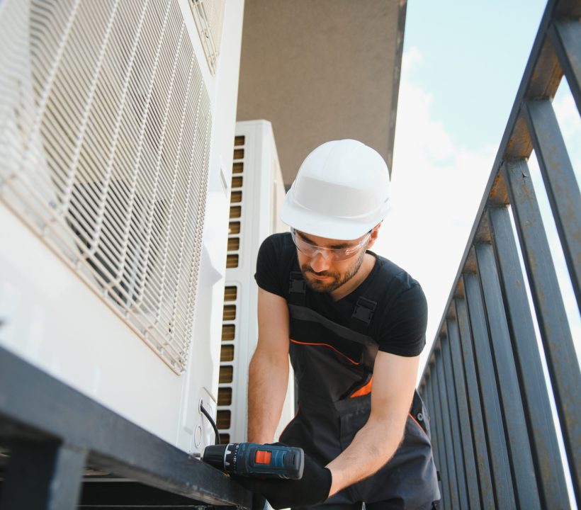 technician working on air conditioning or heat pump outdoor unit. HVAC service, maintenance and repair.